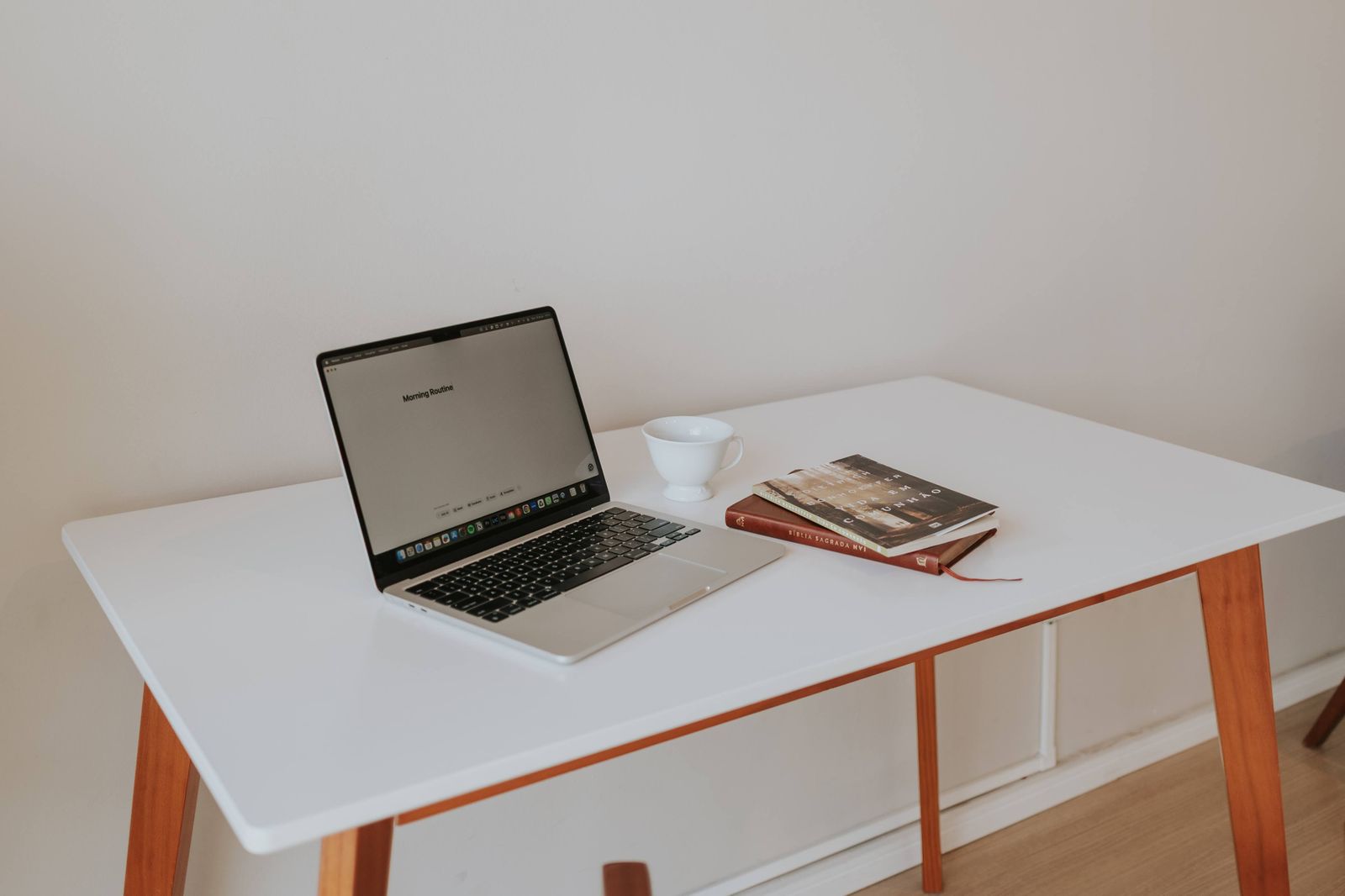 Open laptop on a clean white desk beside a coffee cup and two books