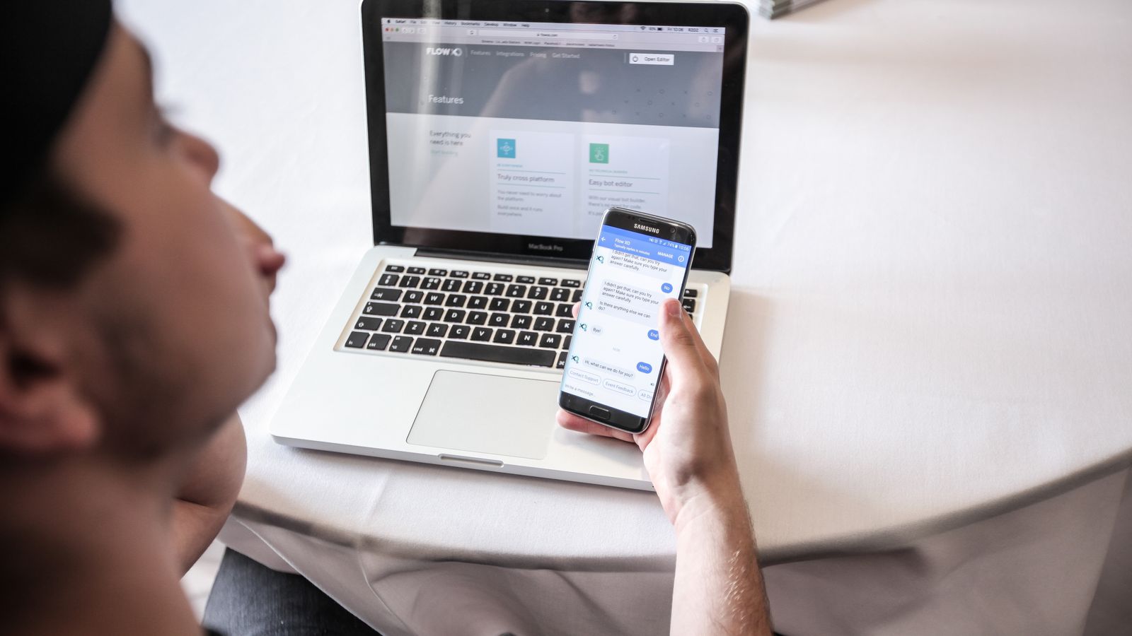 A person building a chatbot on a laptop with a live chat conversation open on a phone beside it