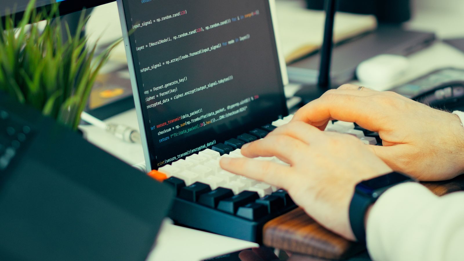 Close-up of hands typing code on a keyboard beside a laptop showing a code editor