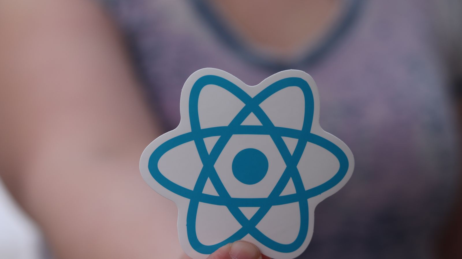 A person holding a React logo sticker, representing building a mobile app with a modern app framework