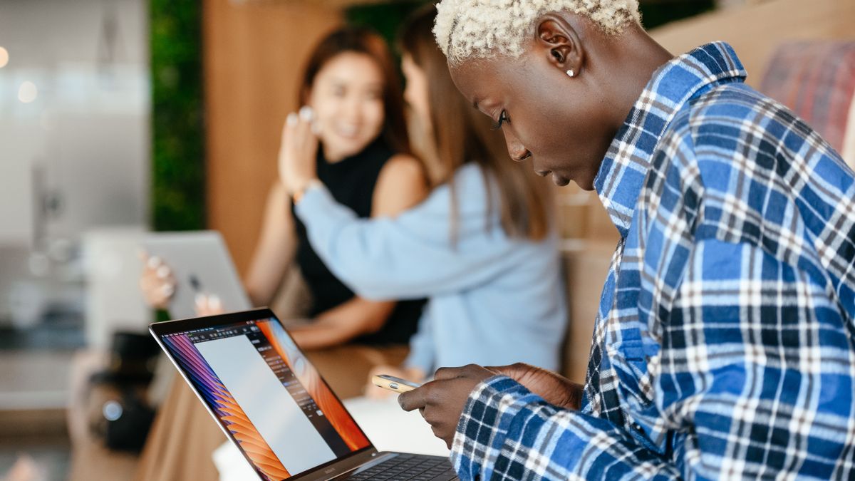 Colleagues working together at a shared table, one messaging on a phone beside a laptop, representing Claude joining a team chat