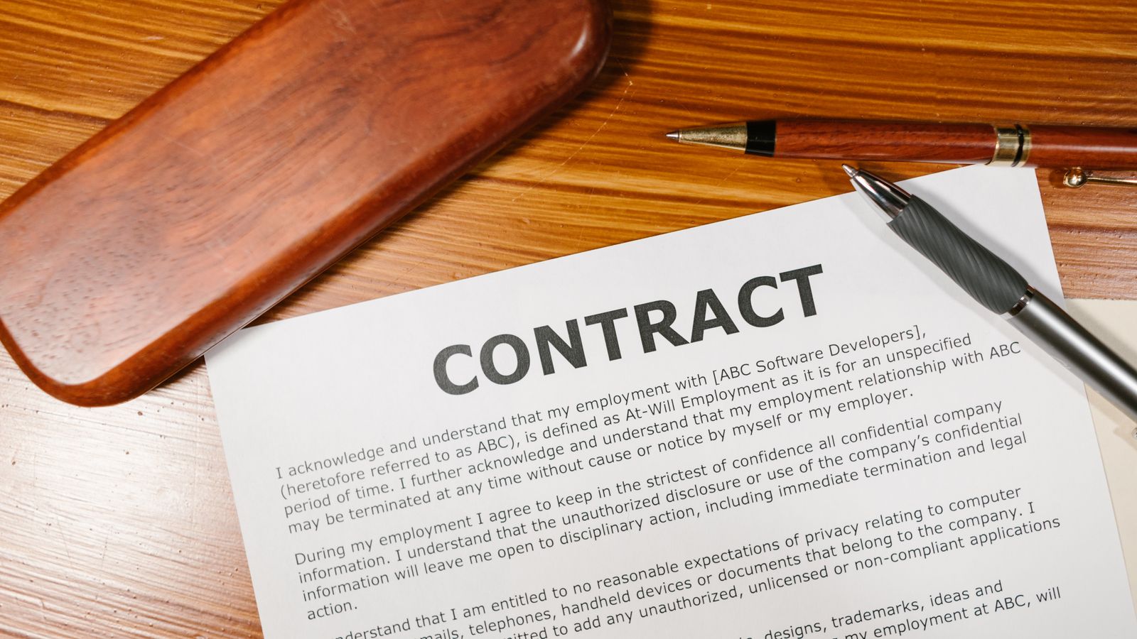 A printed contract and a pen resting on a wooden desk, representing client proposal templates