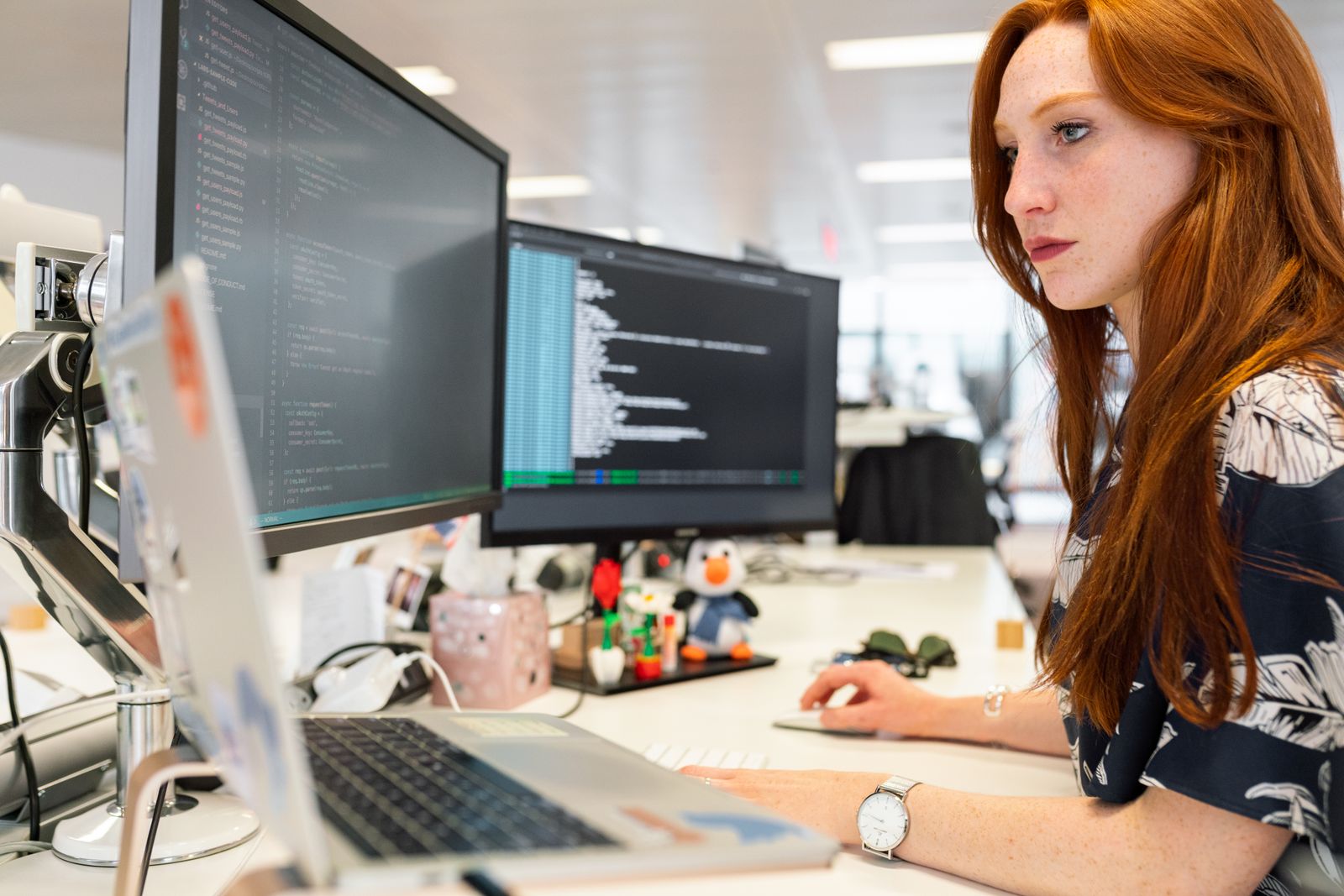 Woman in a soft sweater coding on a laptop with code visible on the screen