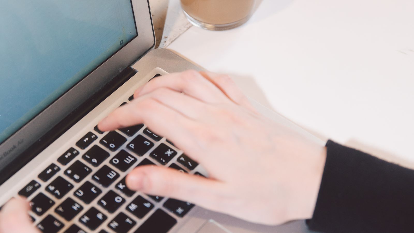 Close-up of hands typing on a laptop at a desk with a coffee