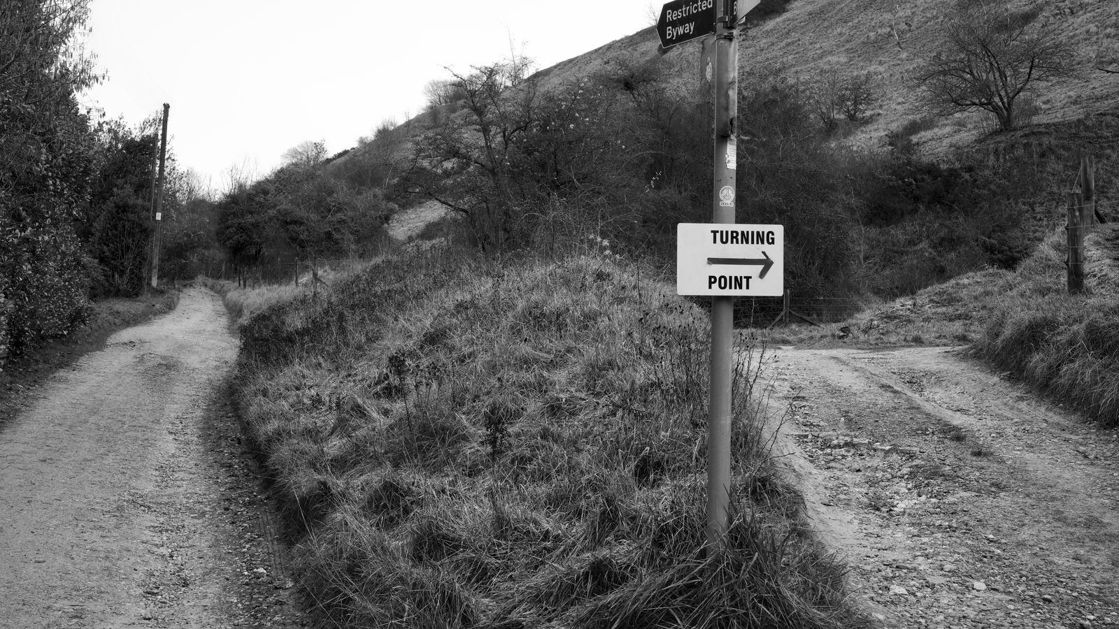 A dirt path splitting into two directions at a signpost, photographed in black and white