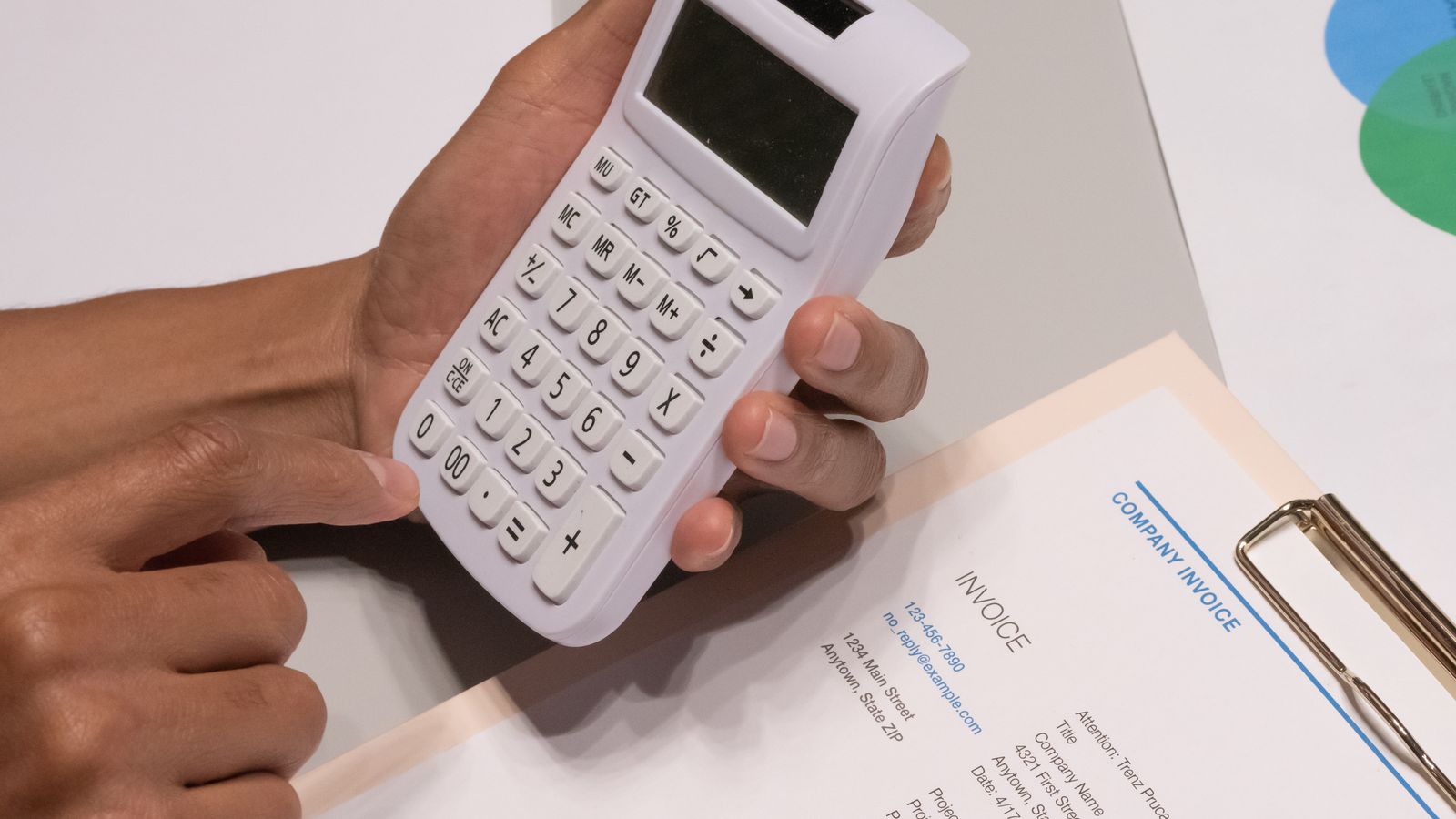 Hands using a calculator next to a company invoice on a desk