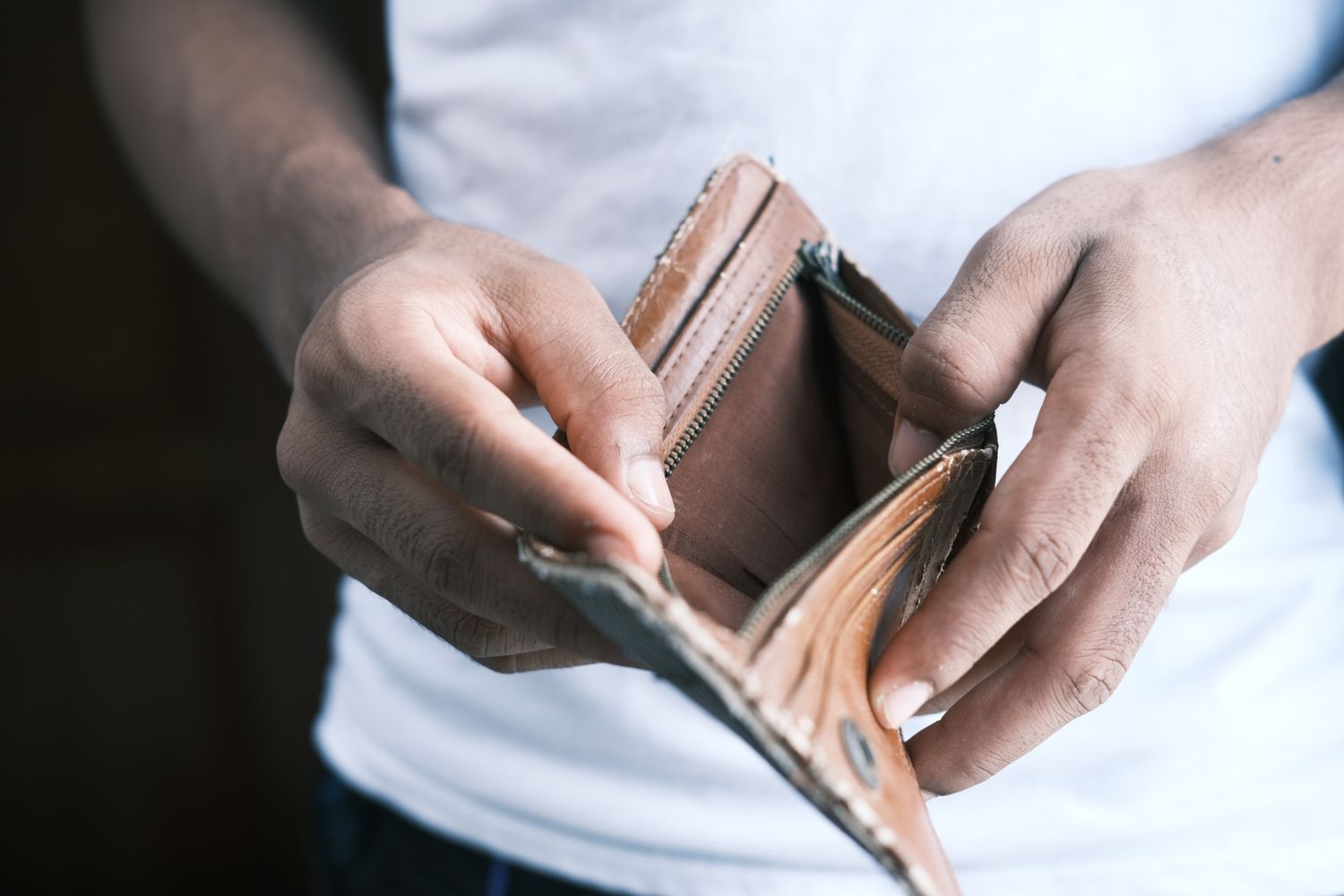 A person holding an open, empty leather wallet with both hands.