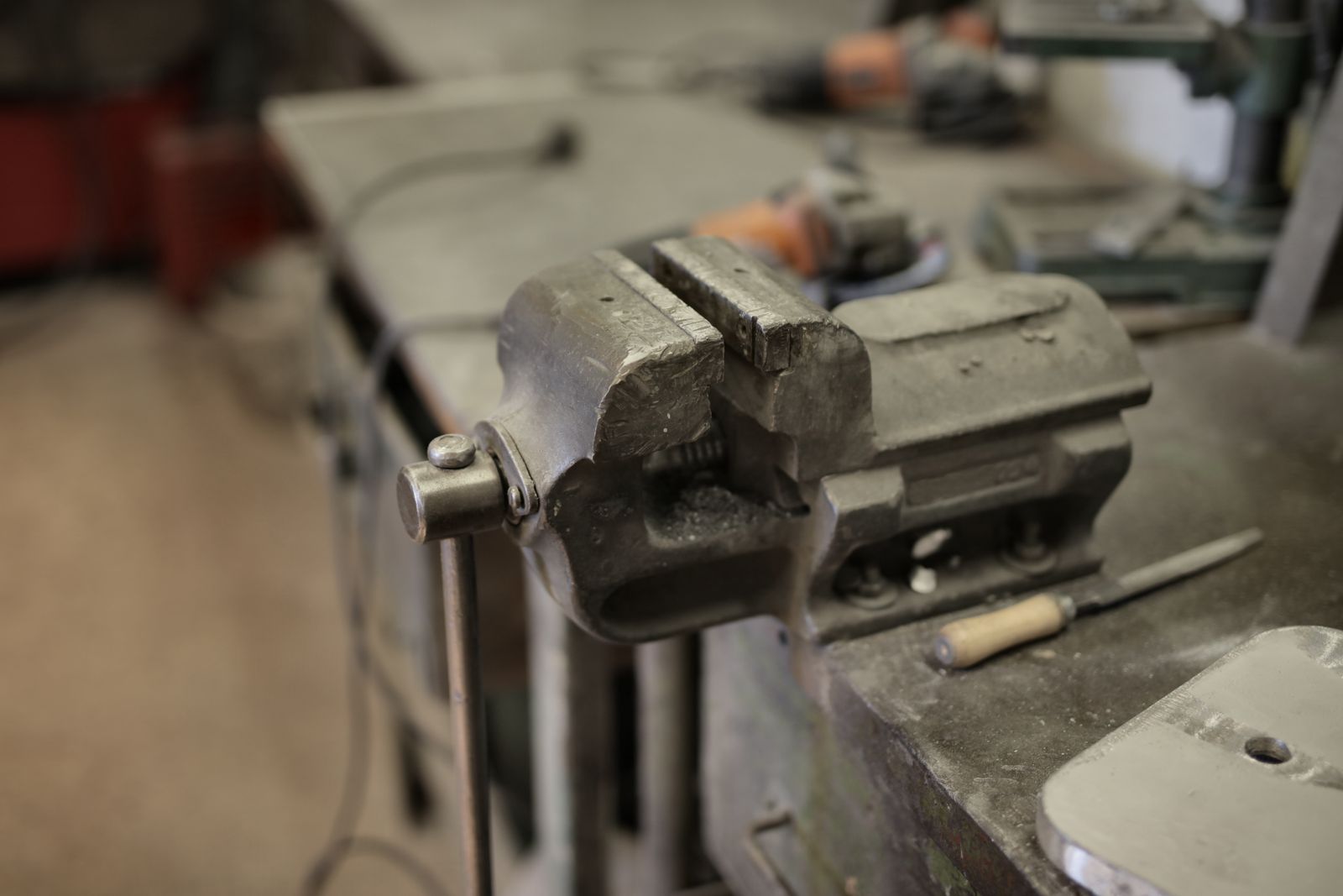 A metal bench vise clamped on a workshop bench beside hand tools