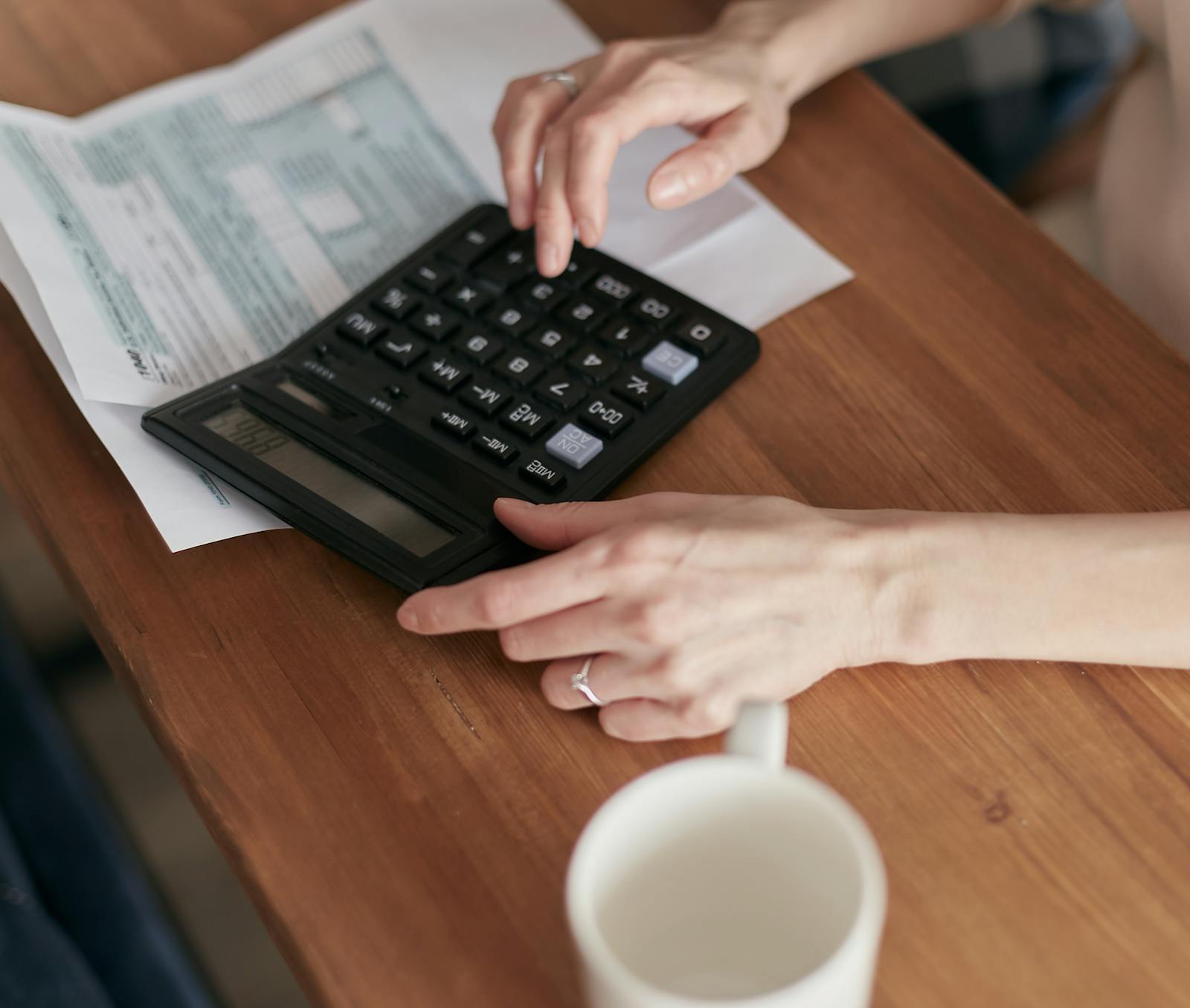 Hands working with a calculator and a notepad on a wooden desk, doing the math on a business decision