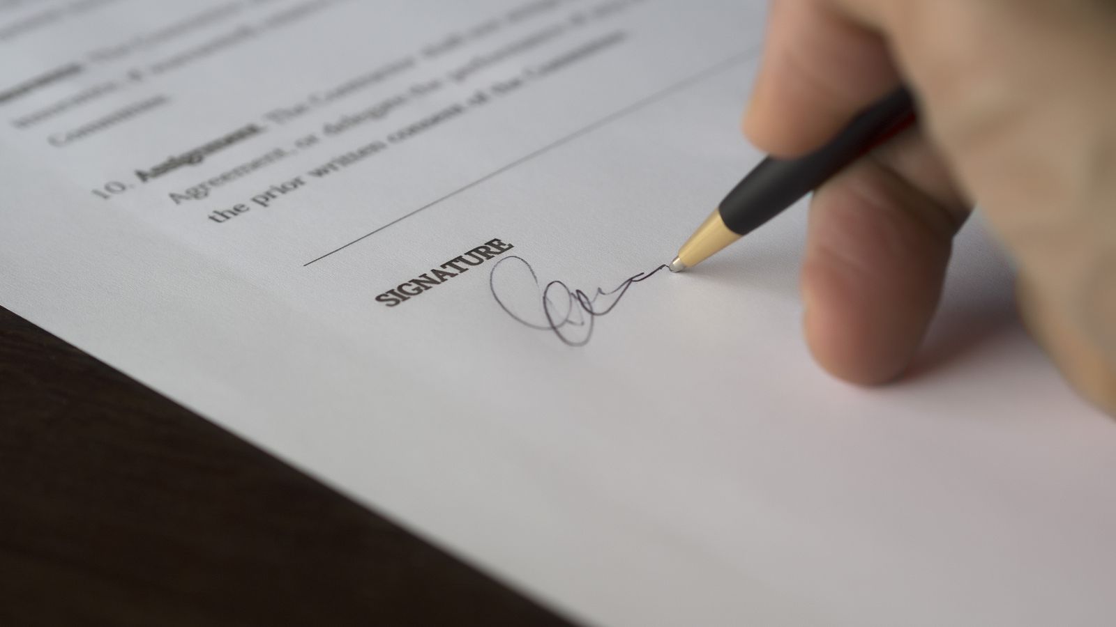 A hand signing a contract on the signature line.