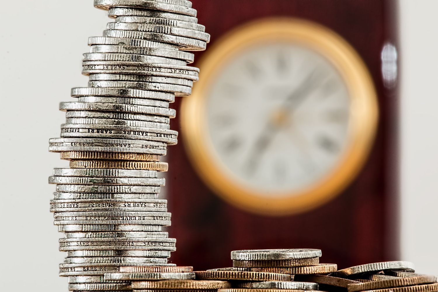 A rising stack of coins in front of an old clock.