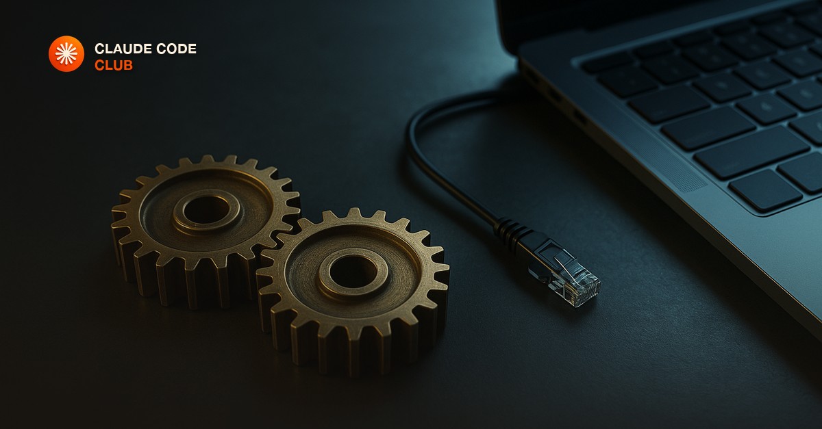 Two meshing brass gears beside a laptop and a patch cable on an industrial desk