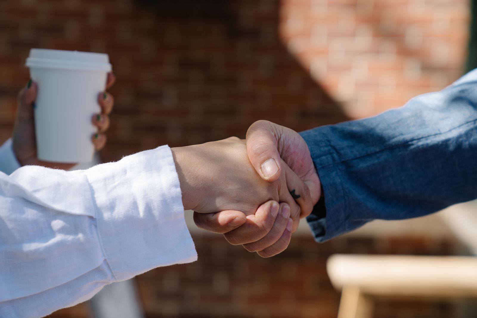 Two people shaking hands over coffee at an outdoor meeting