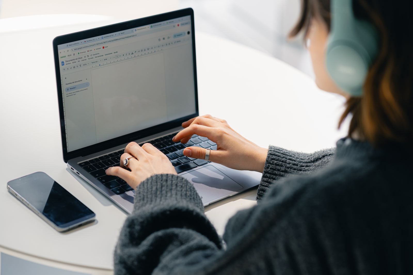 Focused person in headphones writing a message on a laptop at a bright desk